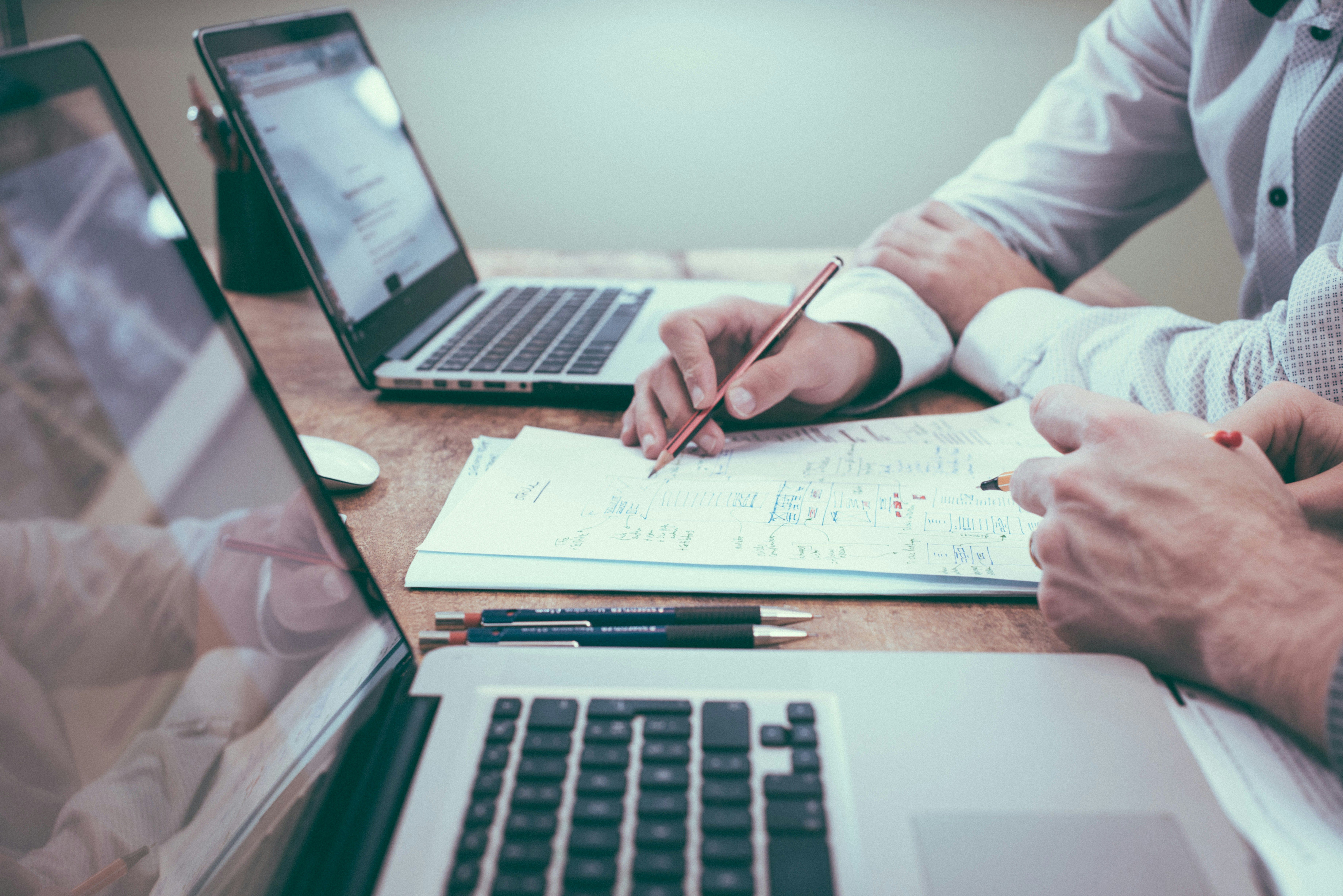 image of two computers and two people looking over a paper in a meeting